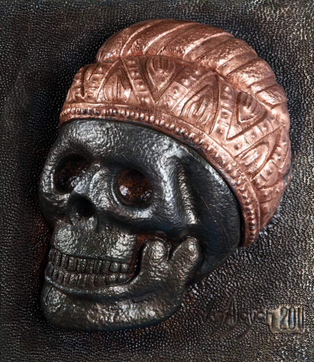Embossed copper and blackened metal relief of a skull wearing a patterned cap